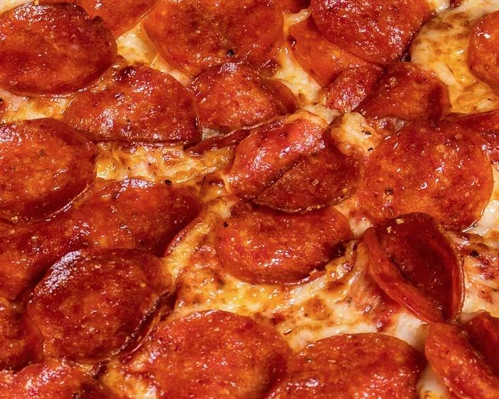 Whole pepperoni pizza on a pan with a golden crust, topped with melted cheese and evenly distributed slices of pepperoni.