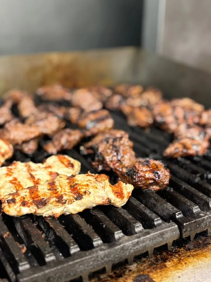 Grilled chicken and beef cooking on a barbecue grill, showcasing a variety of meats with charred grill marks.