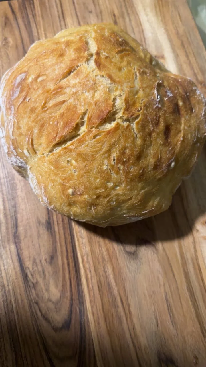 A freshly baked round loaf of bread resting on a wooden cutting board, showcasing its golden-brown crust.