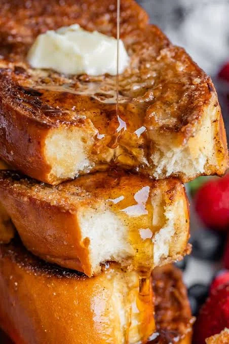 A stack of golden brown French toast topped with a pat of butter and drizzled with syrup.