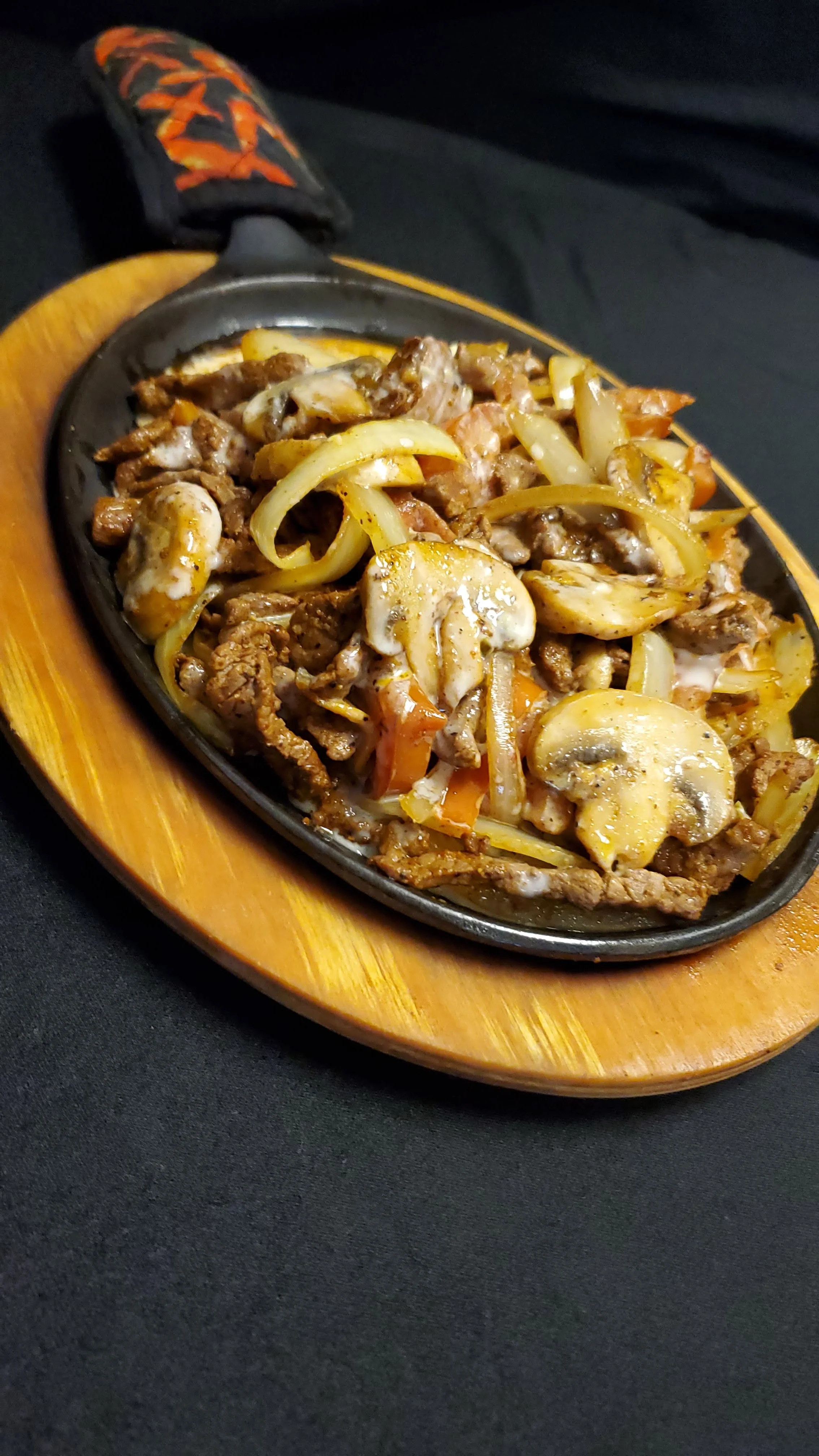 A sizzling skillet of Fajita Roqueta featuring grilled steak strips, onions, mushrooms, tomatoes, and topped with creamy cheese sauce, all perfectly seasoned and served hot. The best fajita in Radford.