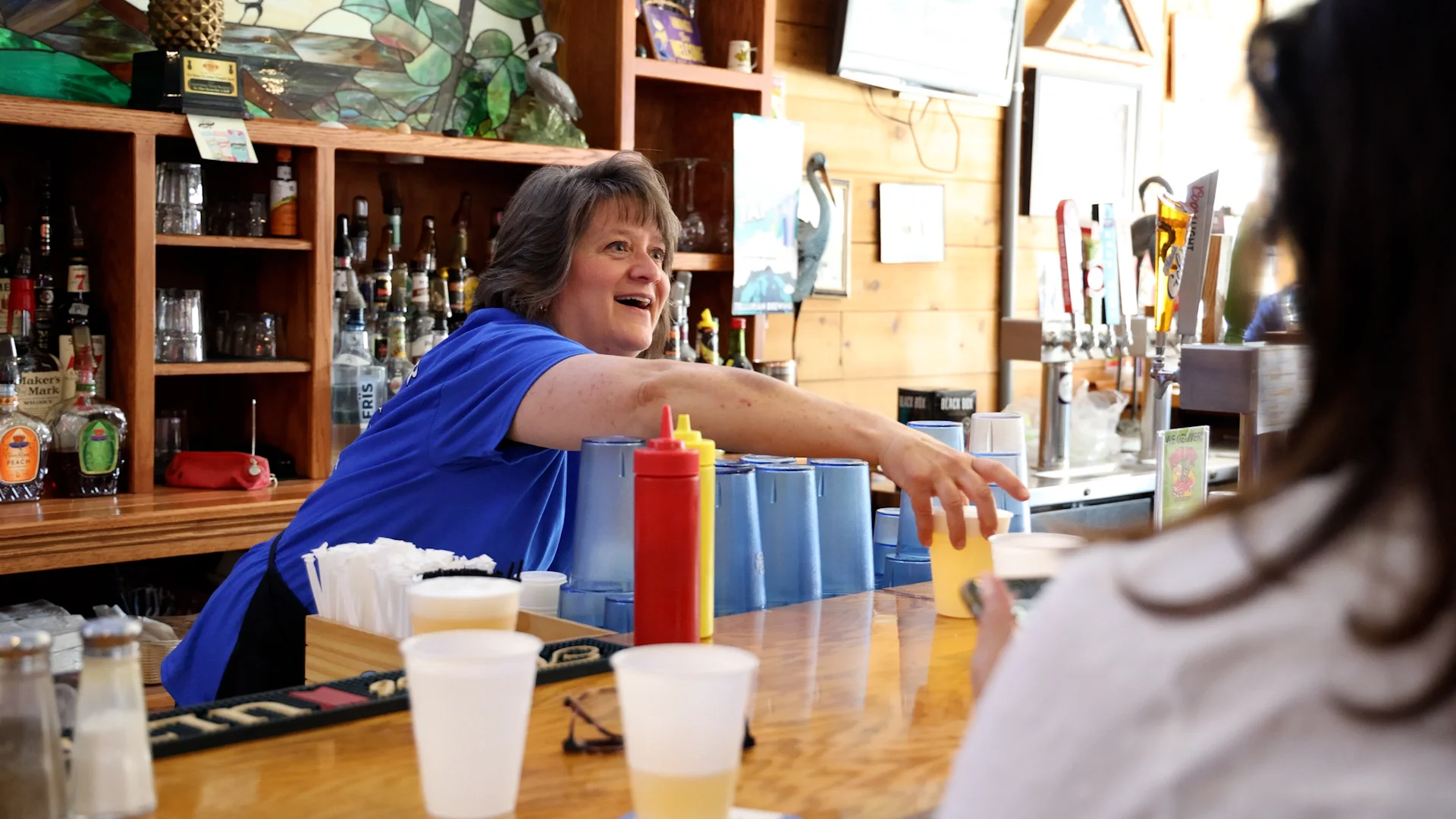 Bartender serving drinks at a lively bar with colorful decor.