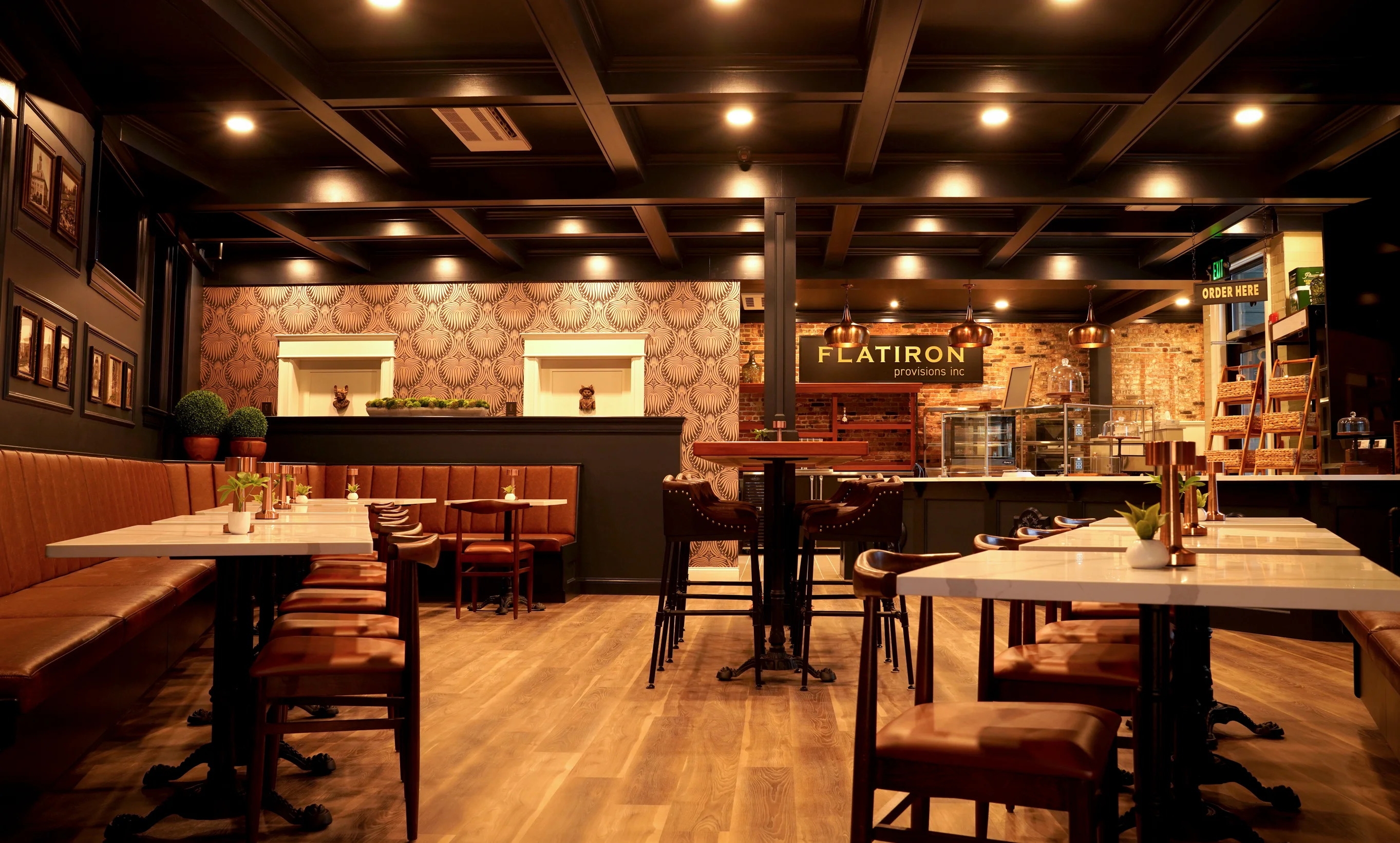 Dining room and order counter inside Flatiron Provisions Inc. restaurant, showcasing cozy booth seating, coffered dark wood ceilings, and exposed brick decor.