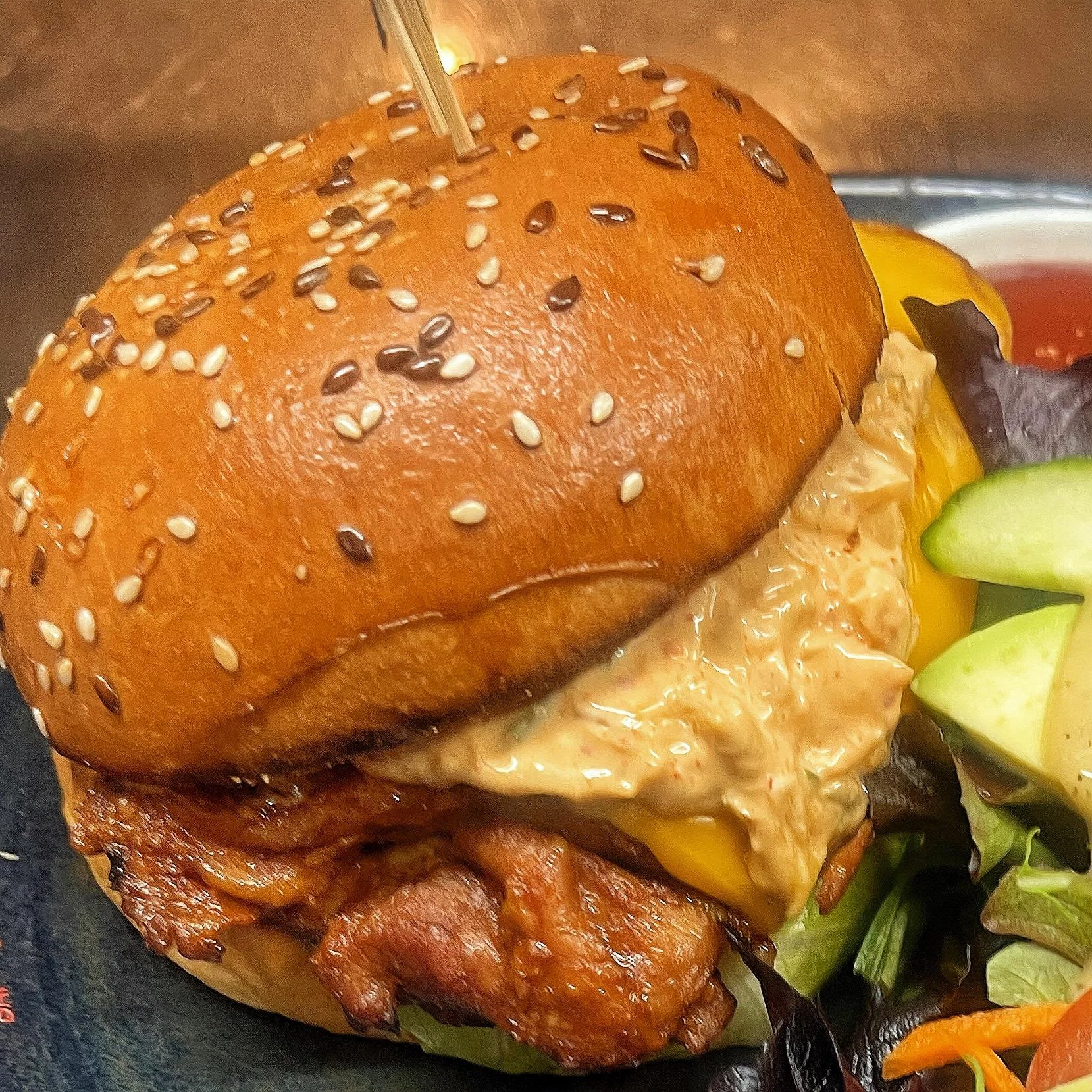 A delicious chicken burger topped with a rich sauce and cheese, served in a sesame seed bun. Includes a side salad.