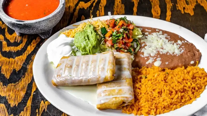 Plate of enchiladas with rice, beans, and fresh toppings.