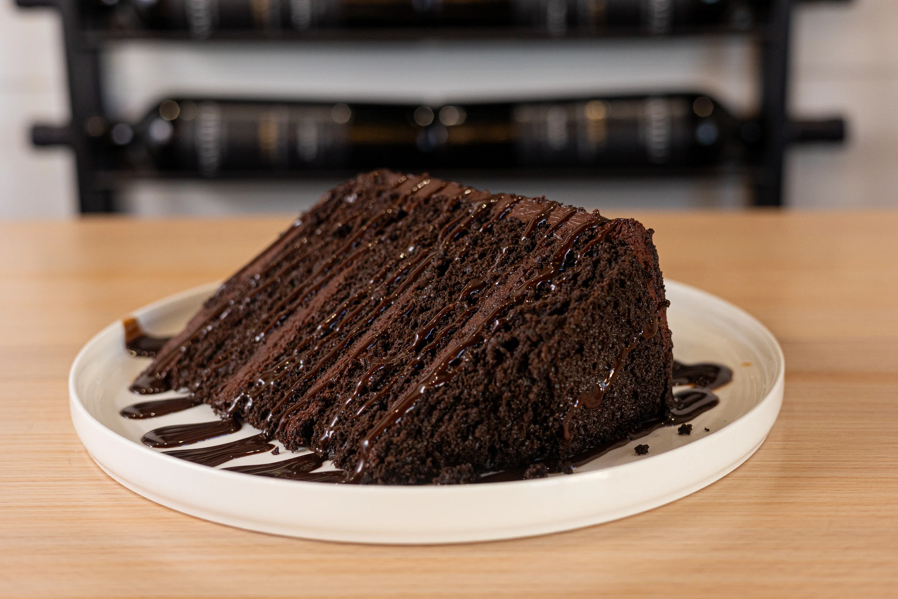 A slice of rich chocolate cake drizzled with chocolate sauce on a plate.