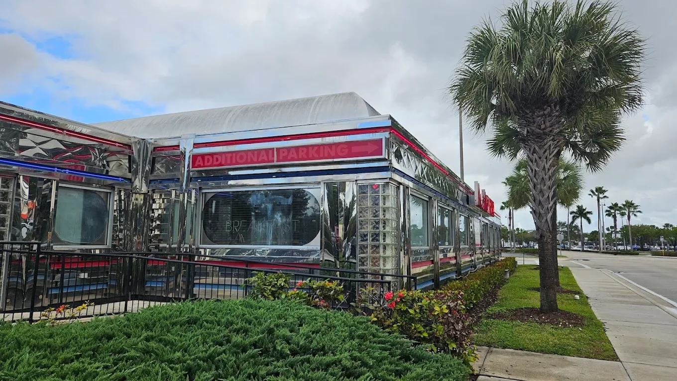 Exterior corner view of Moonlite Diner featuring its iconic retro stainless steel design, palm trees, and classic American diner atmosphere in South Florida.