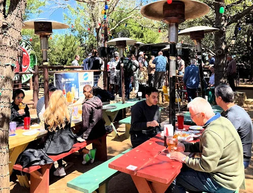 Lively outdoor restaurant patio with diners, fire pit, and string lights