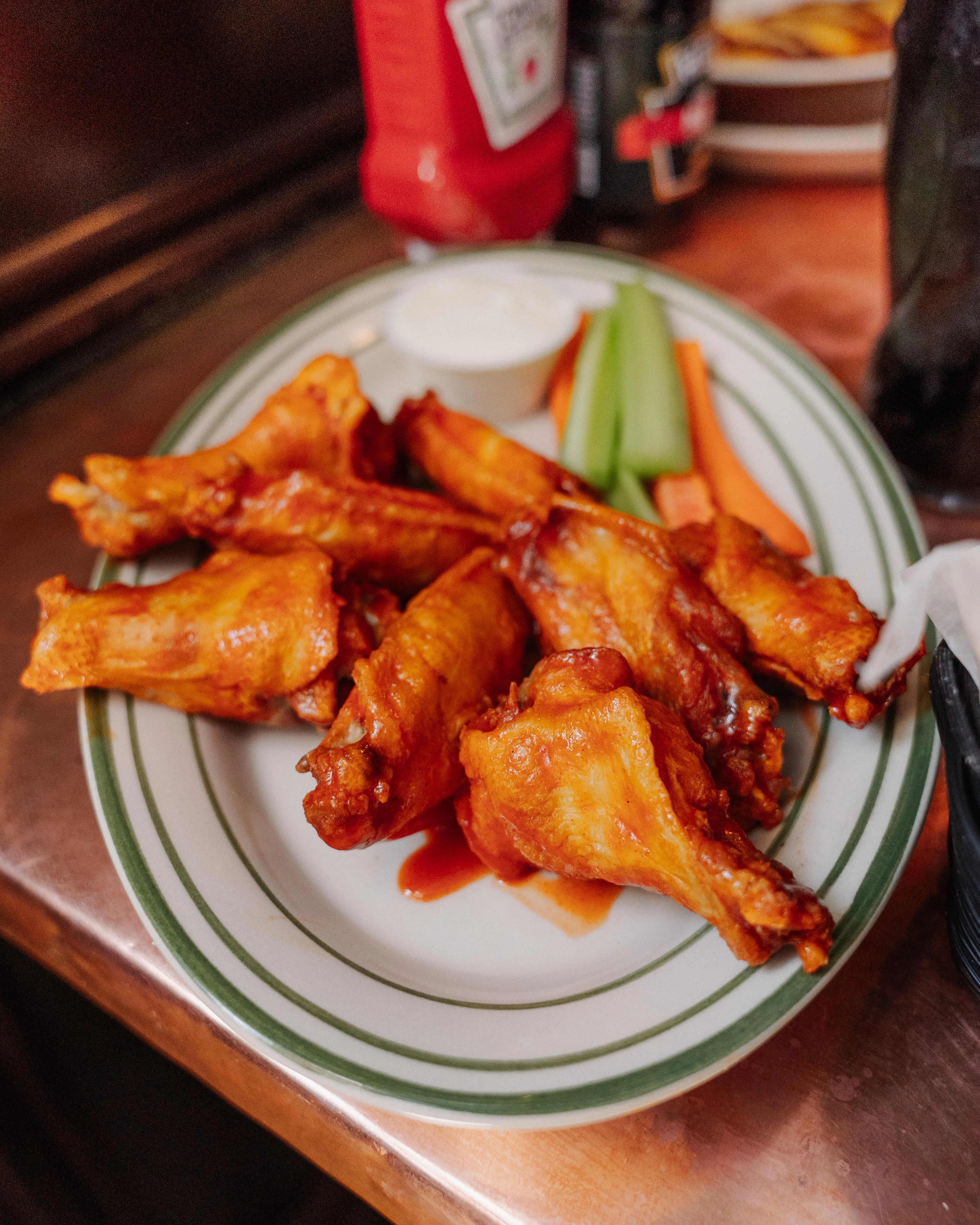 A plate of crispy chicken wings glazed with sauce, accompanied by celery, carrots, and a small cup of white dressing.