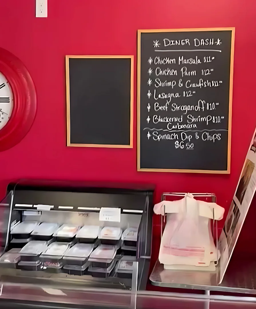 Cooler with take and bake meals next to Diner Dash chalk menu board on wall with various meals and their prices all at TJ's Sandwich Shop