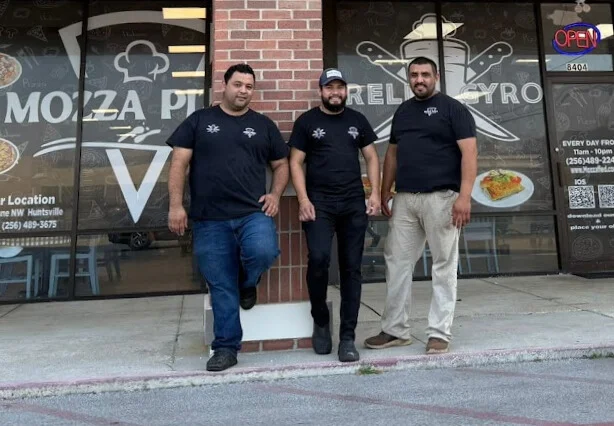 Three restaurant staff members outside a pizzeria and gyro shop