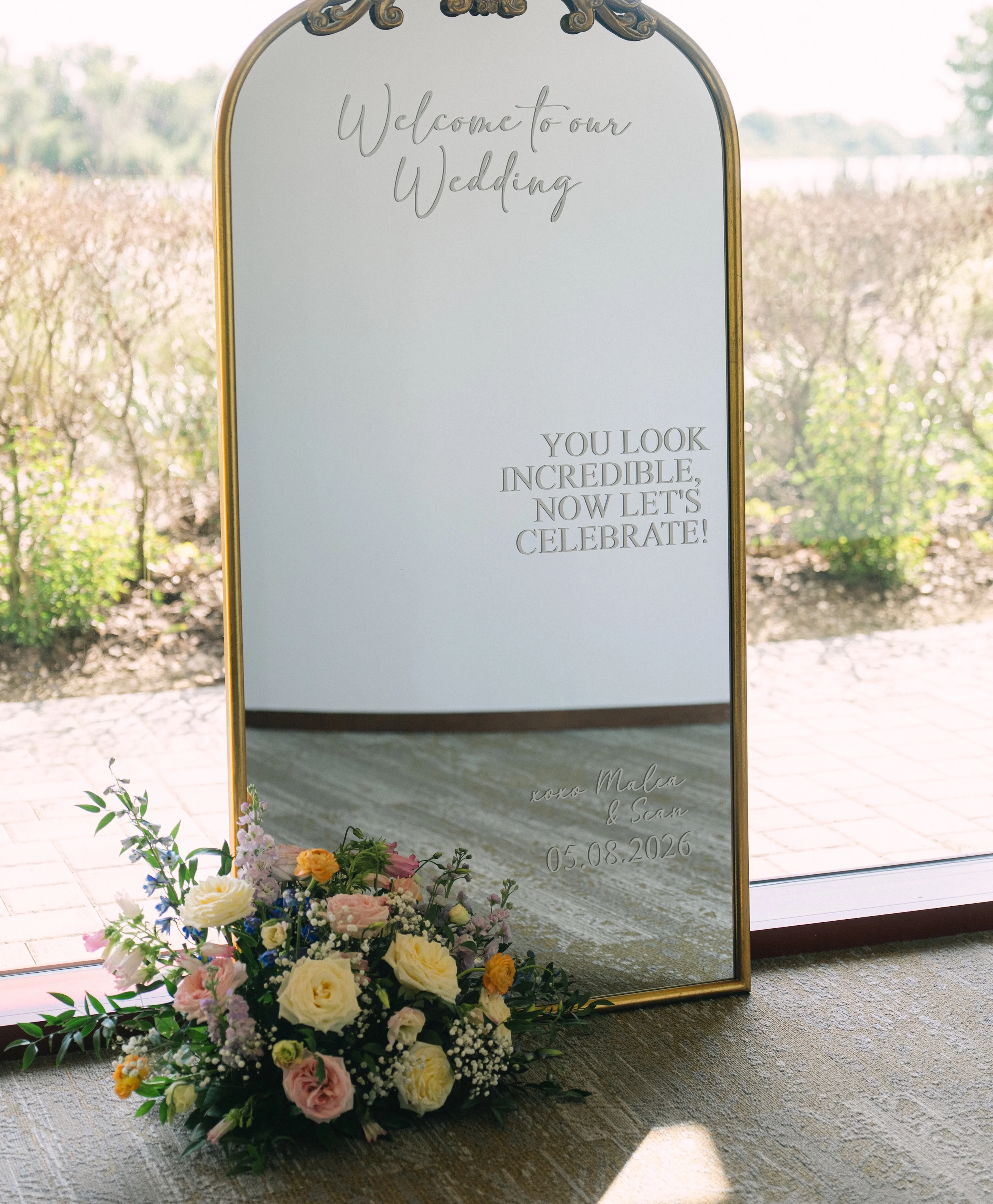 Elegant wedding mirror with floral arrangement and welcoming message