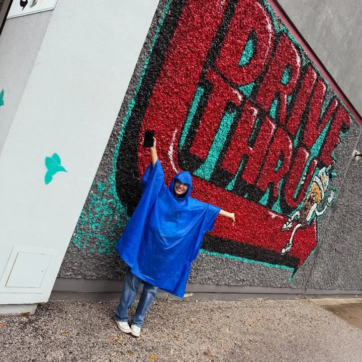 Person in blue poncho posing by colorful drive-thru mural