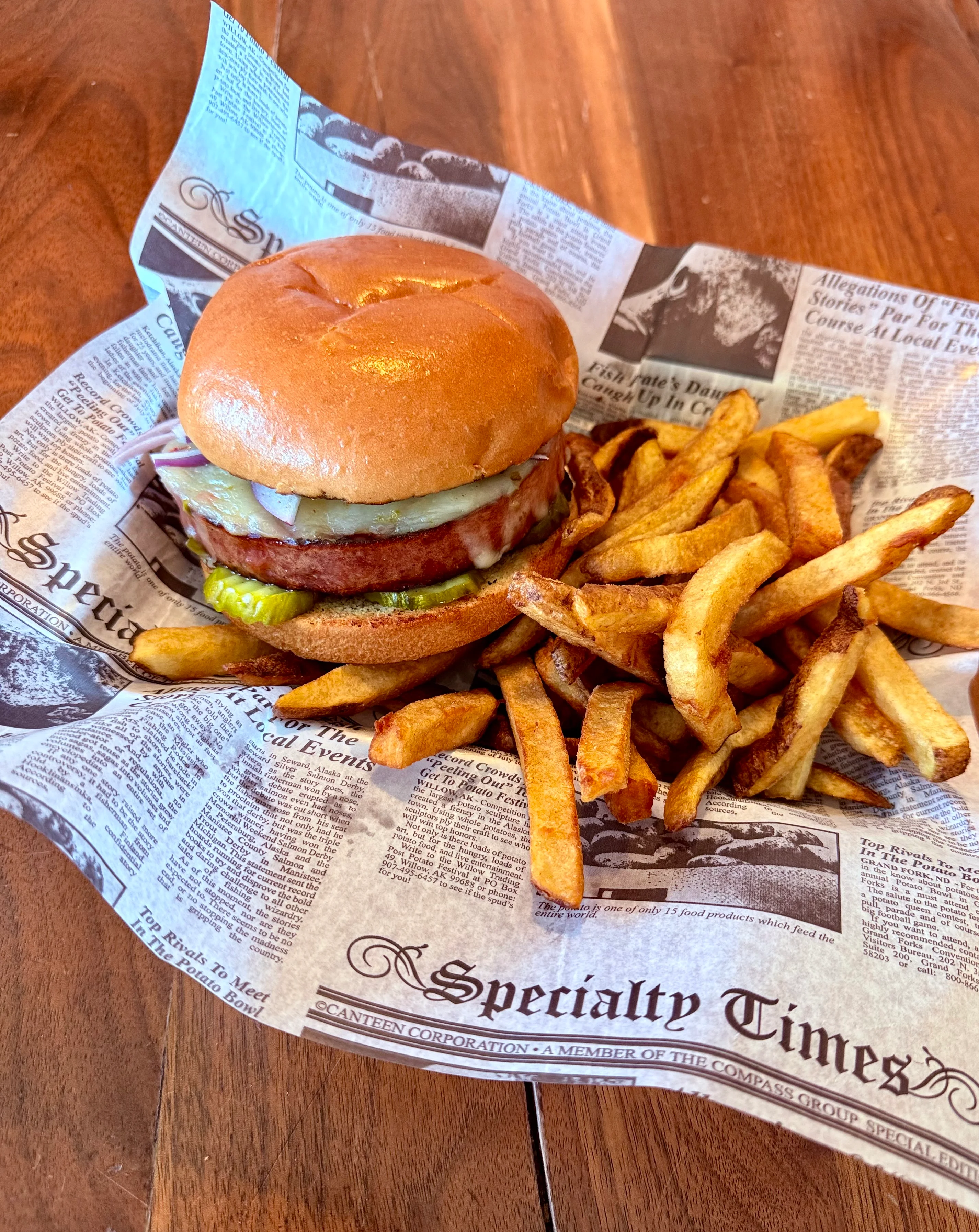 A delicious burger served on newspaper with a side of golden French fries, all presented on a wooden table.