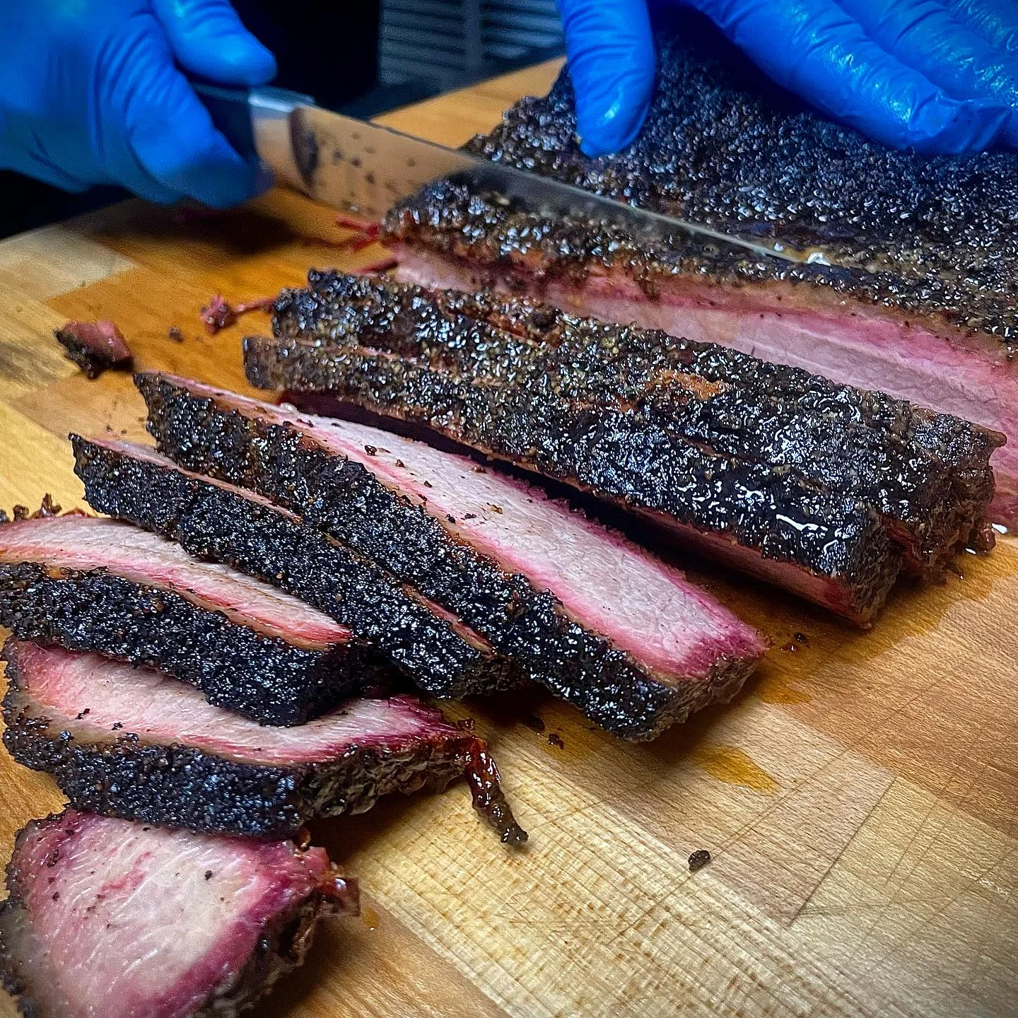 Sliced brisket on a wooden cutting board, showcasing a well-seasoned and smoky bark with a juicy cross-section visible in the slices.
