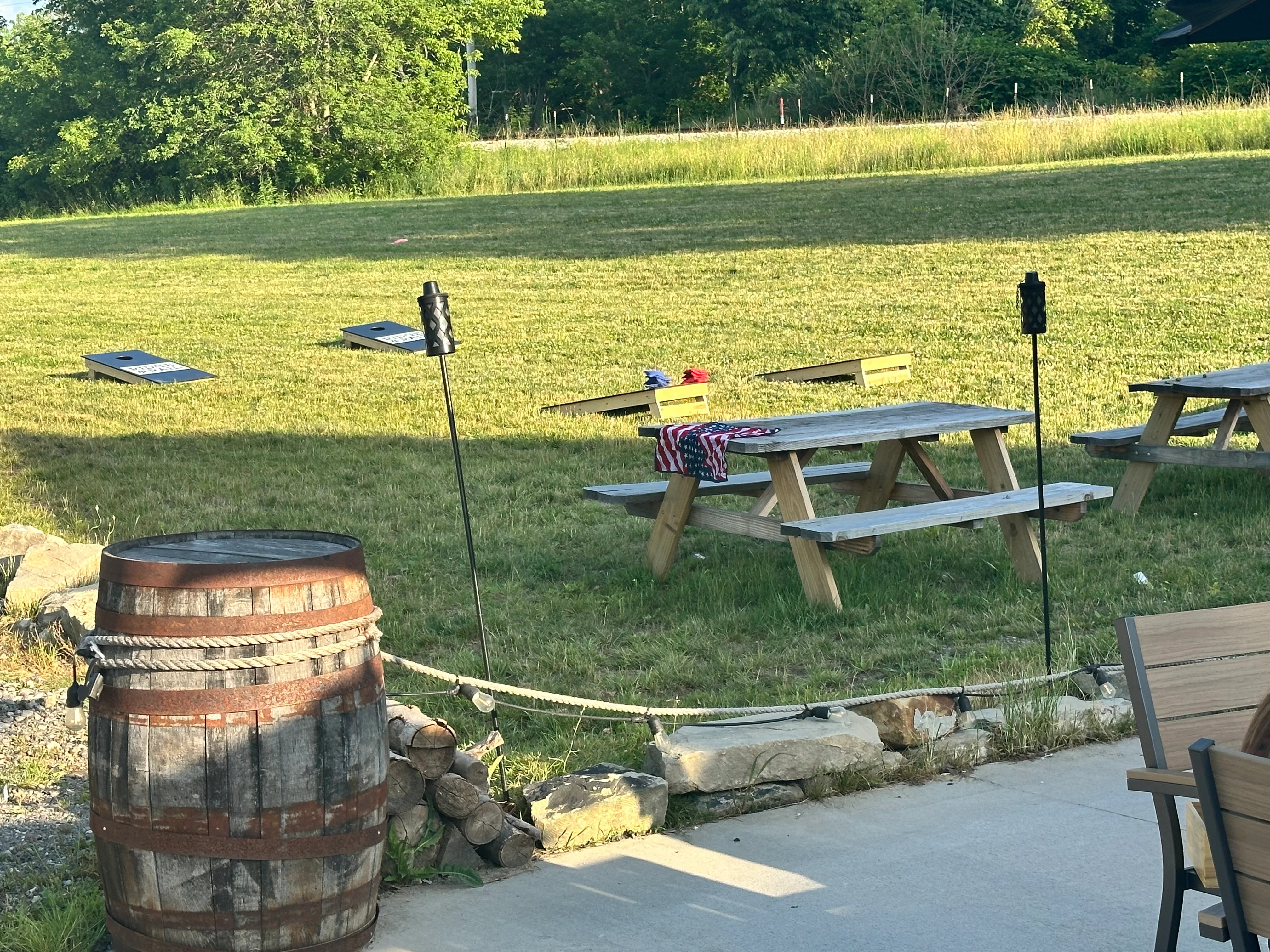 An outdoor area featuring picnic tables, cornhole boards, and a grassy field, perfect for gatherings.