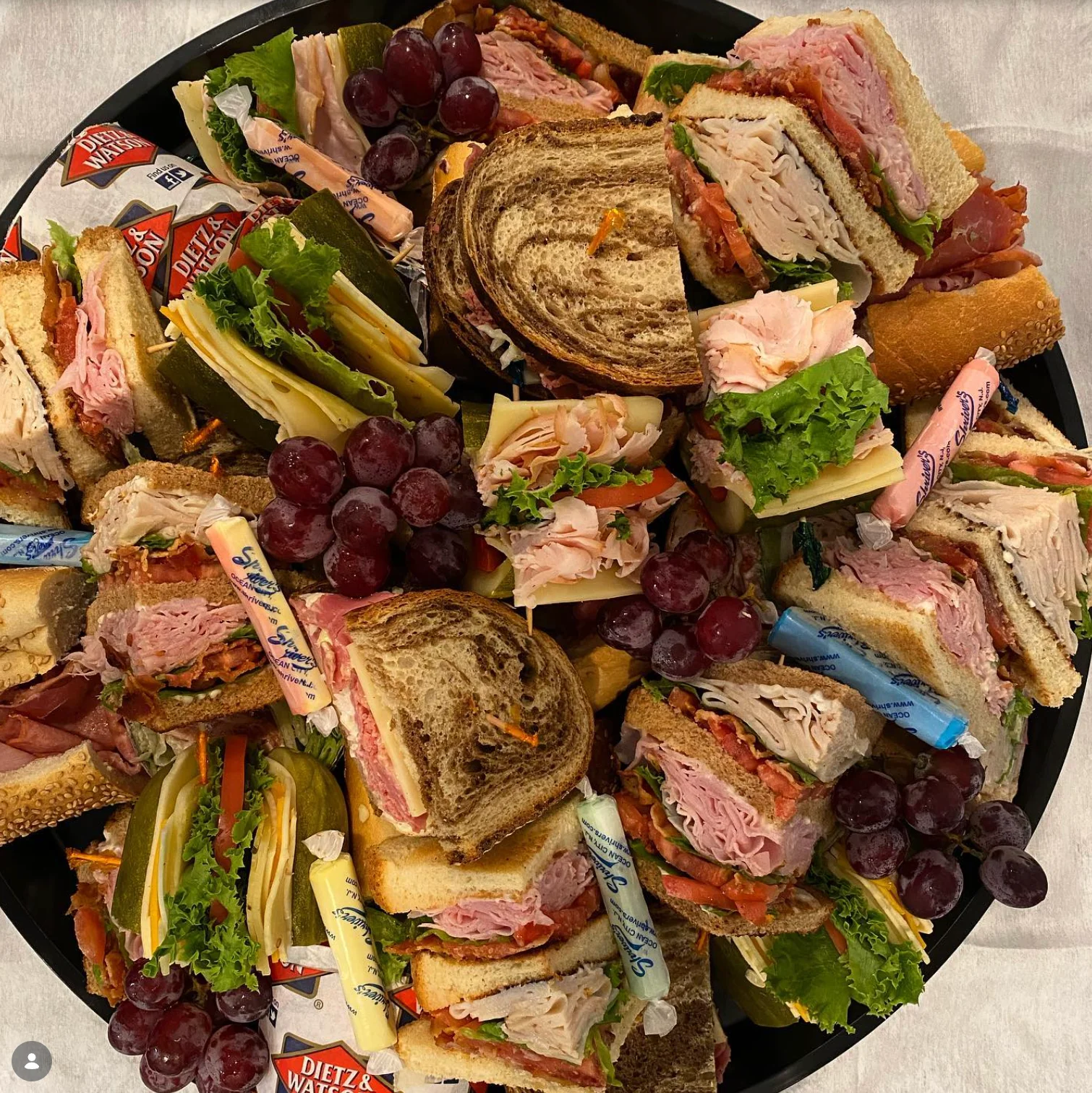 A variety of sandwiches stacked together, featuring meats, lettuce, and pickles.