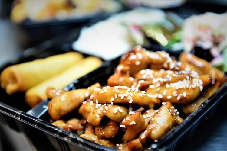 Sesame chicken with spring rolls in a Chinese takeout box