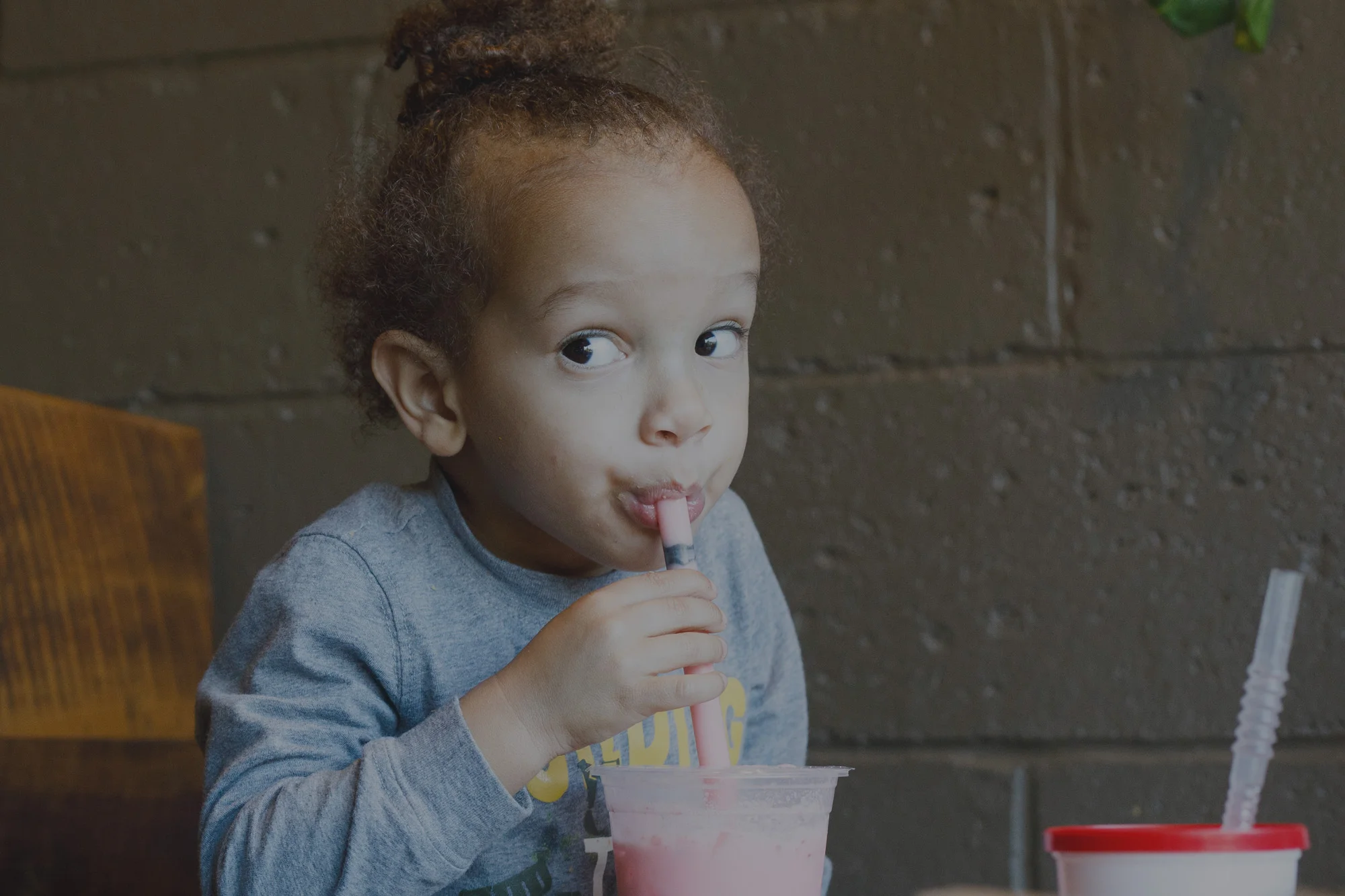 Child enjoying a pink milkshake in a cozy cafe
