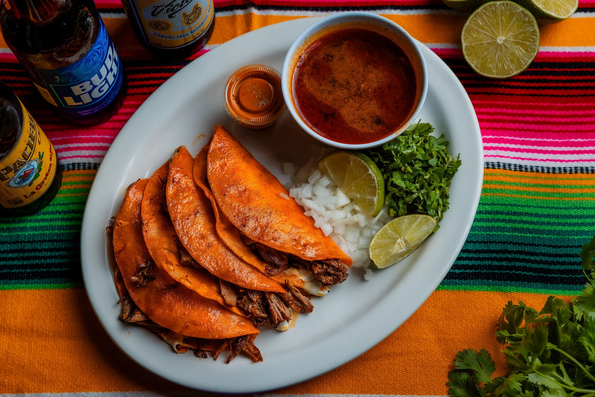 Plate of Mexican tacos with consomé and fresh toppings