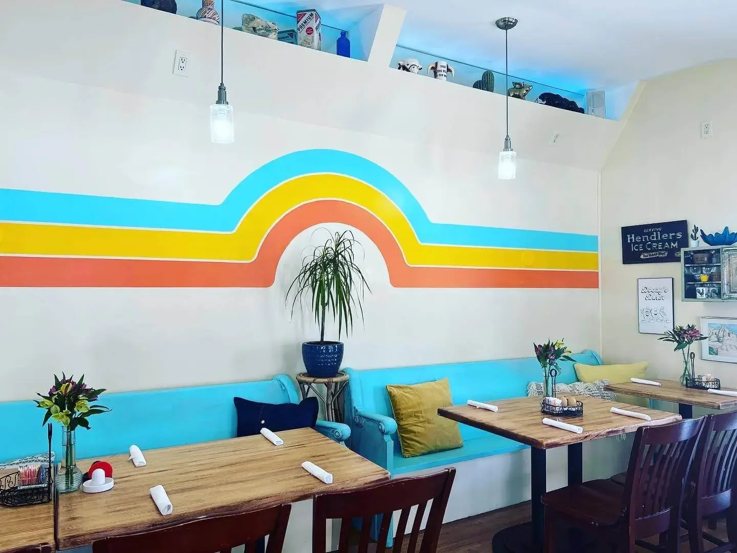 Image of the main dining room at Doozy's Diner, featuring a retro stripe pattern on the wall, tables set with roll ups, bright and cheery decor.