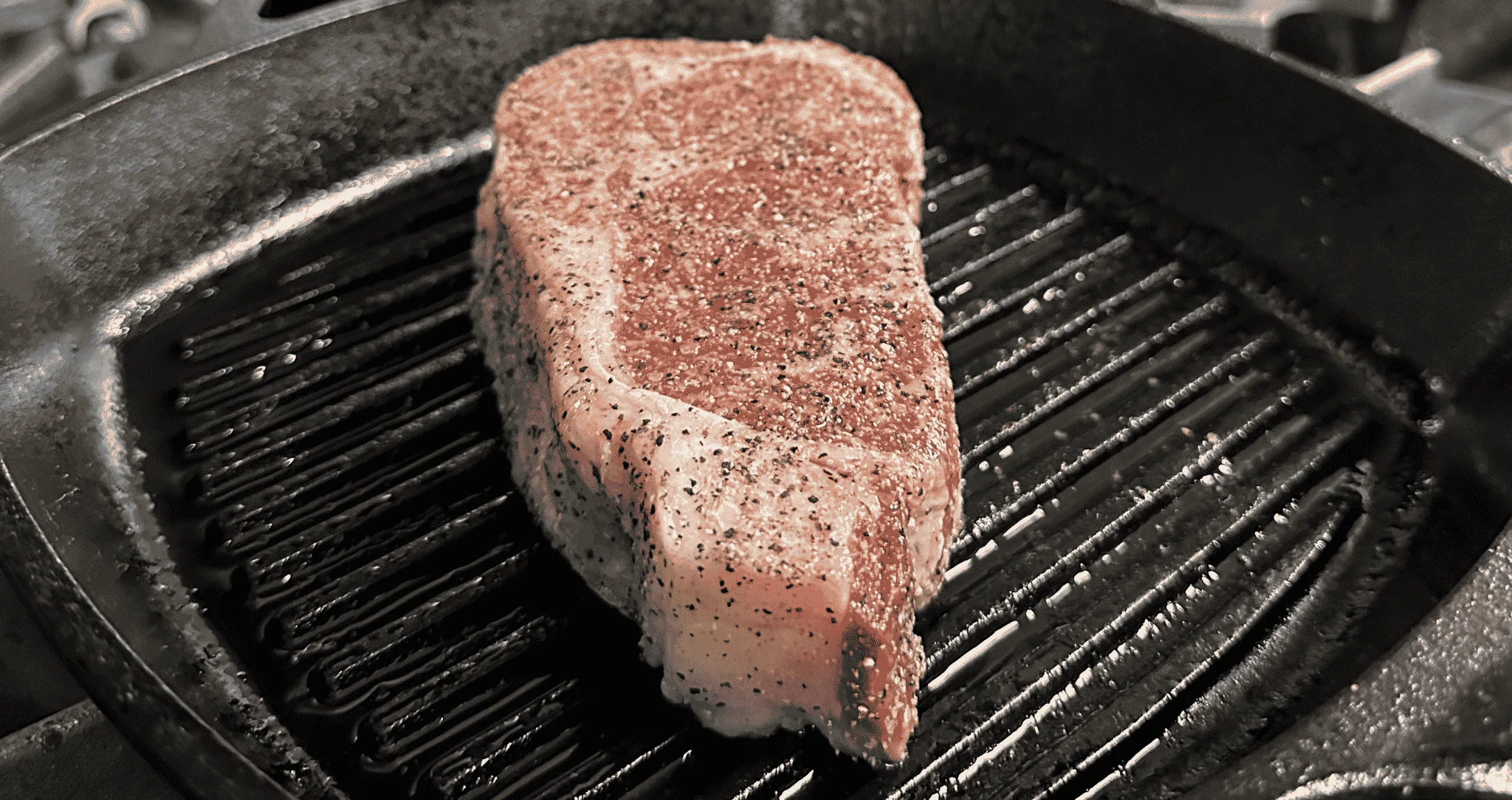 A seasoned steak cooking on a grill pan.