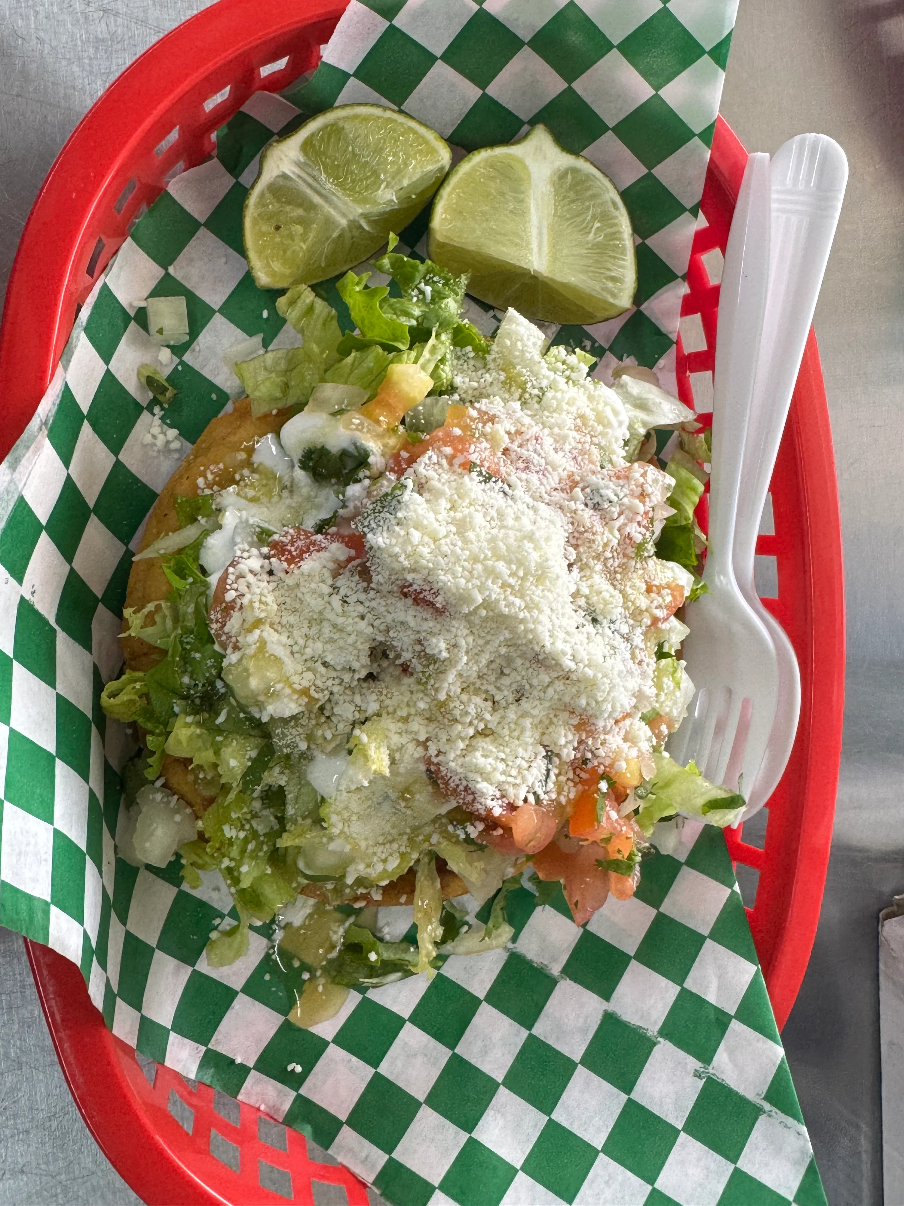 A basket containing a salad with lettuce, tomato, and cheese, accompanied by lime wedges.