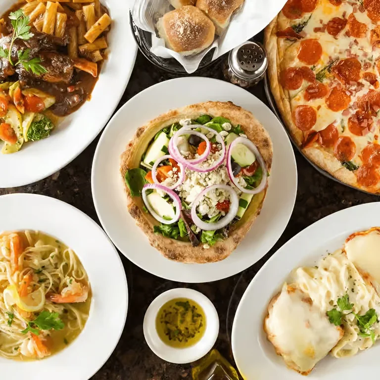 Assorted Italian dishes including a fresh vegetable pizza, pepperoni pizza, pasta, soup, and entrée plates arranged on a dining table.