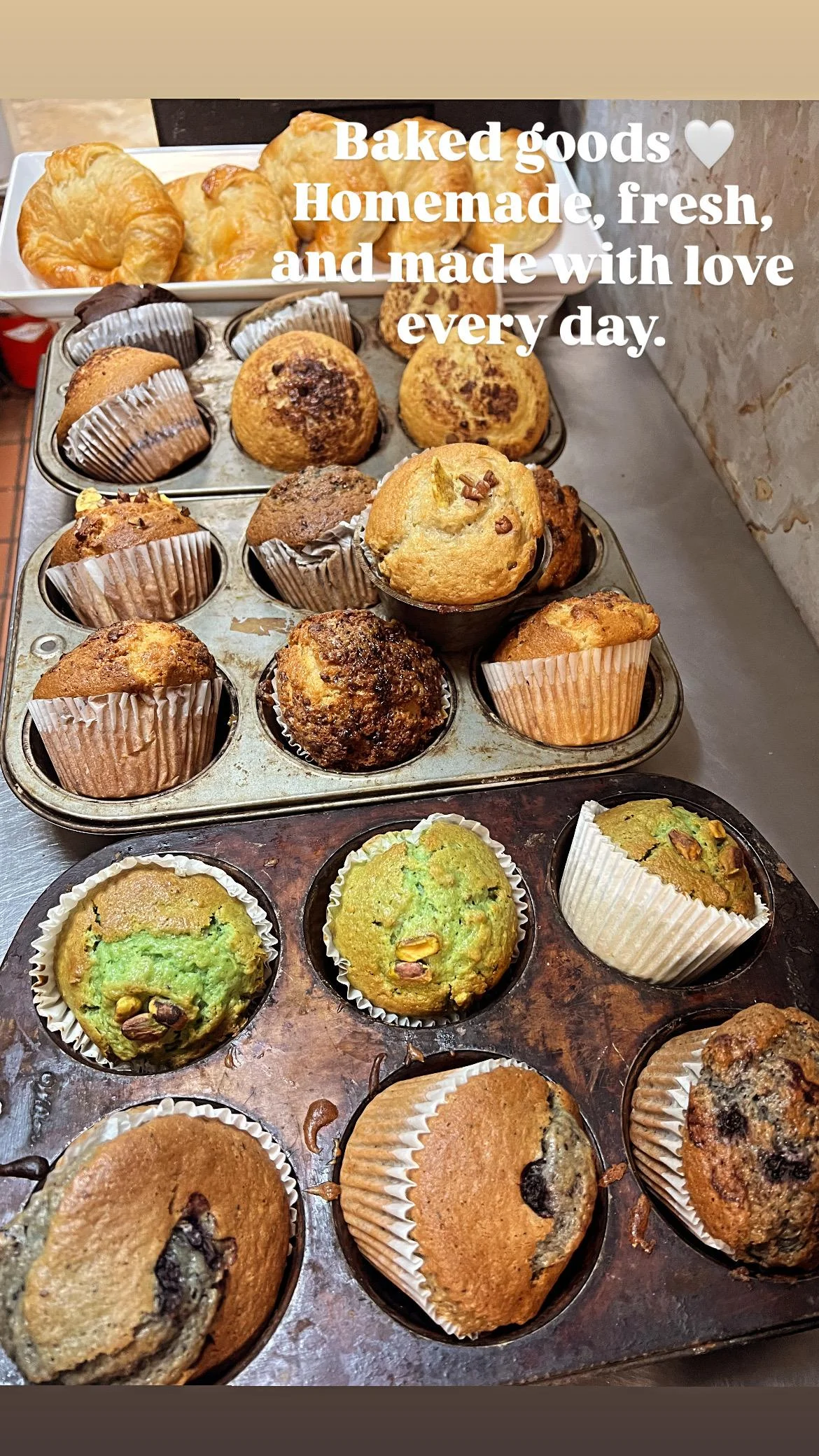 A variety of muffins in a tray, including flavors like blueberry, chocolate, and green-colored muffins.