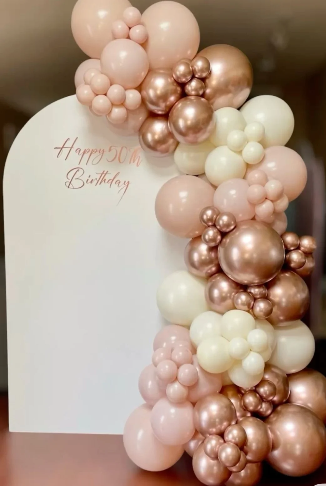 A festive balloon arrangement featuring shades of pink, white, and bronze, along with a sign that reads 'Happy 50th Birthday'.