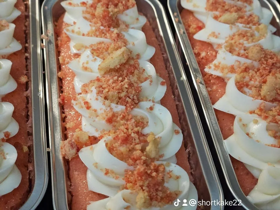 Close-up of dessert loaves topped with whipped cream and colorful crumbs, showcasing a vibrant orange layer.