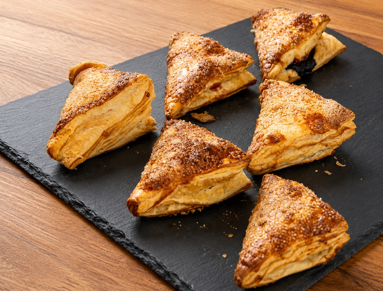 Golden-brown pastry triangles with a sugary topping on a slate board.