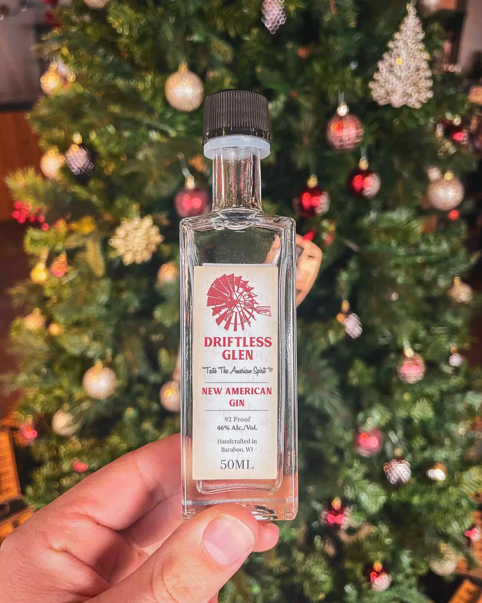 An image of a 50 ml bottle being held in front of holiday decorations
