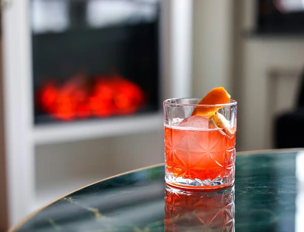 A vibrant cocktail with ice and an orange twist on a marble table.
