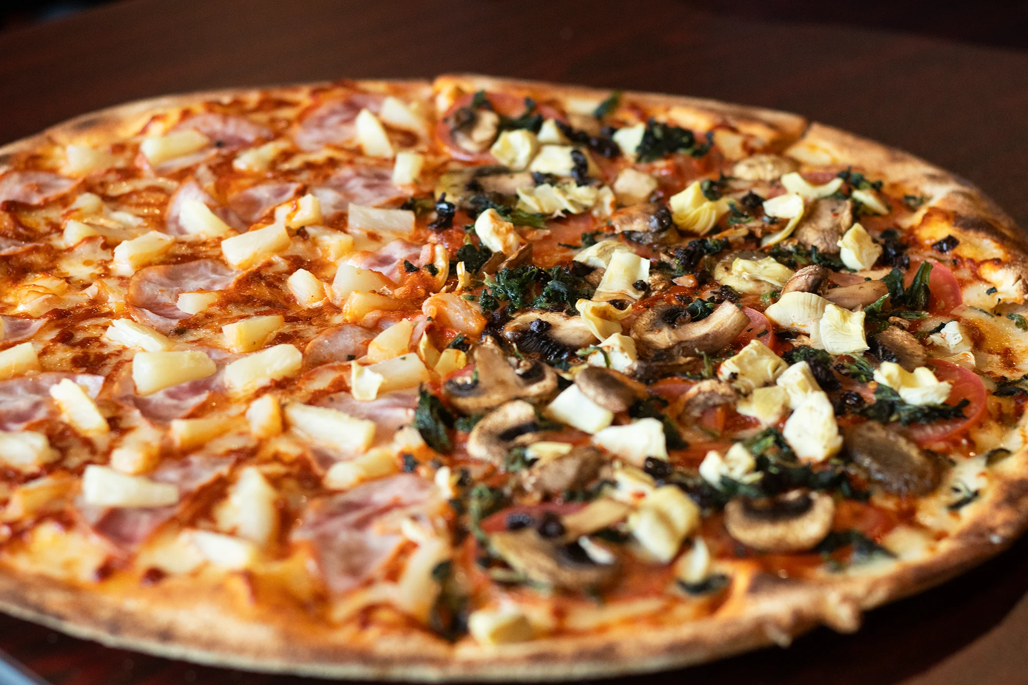 Half Hawaiian pizza and half vegetarian pizza on a wooden table