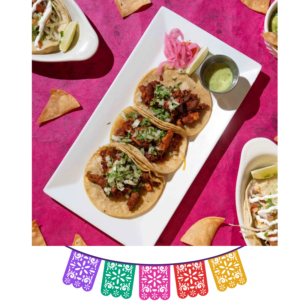 Three tacos topped with cilantro and onion, served with salsa and pickled onions at Friducha in Brooklyn, NY.