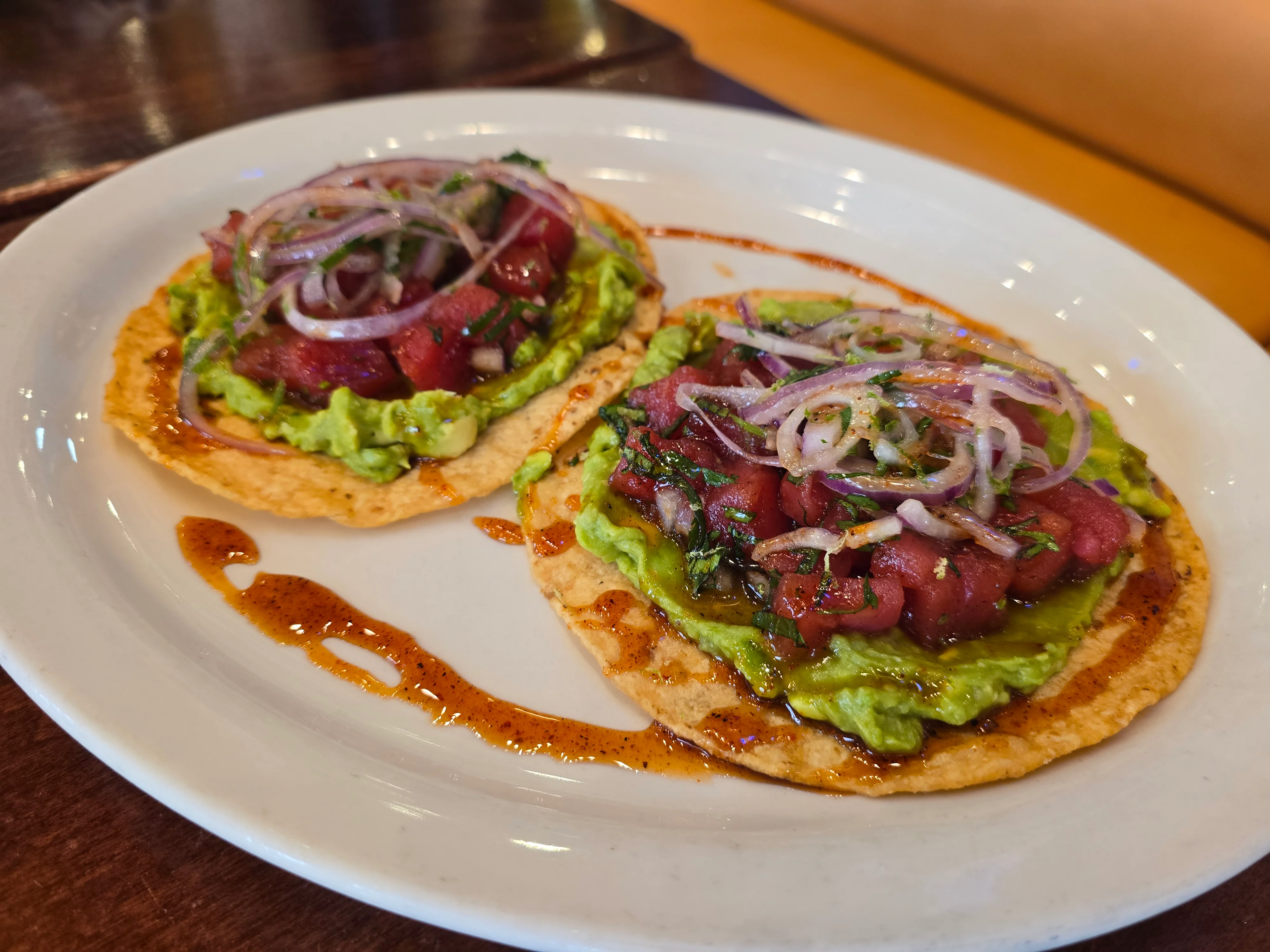 Two tostadas topped with guacamole and diced tuna, garnished with onions.