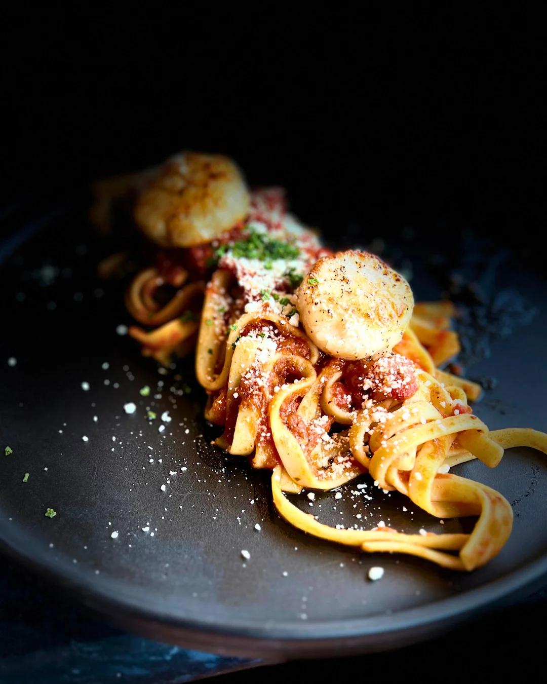 Plate of fettuccine pasta topped with scallops and cheese.