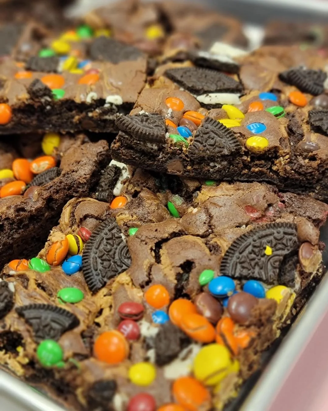 Trays of brownies, some topped with nuts, others with colorful candies and Oreo pieces.