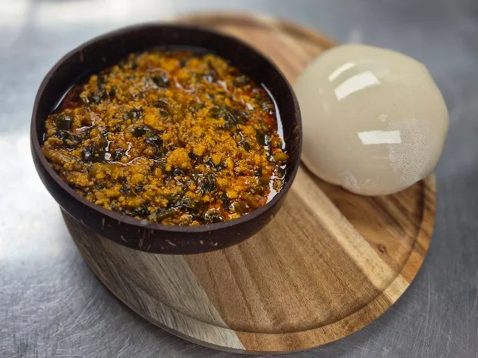 Nigerian egusi soup served with fufu on a wooden platter