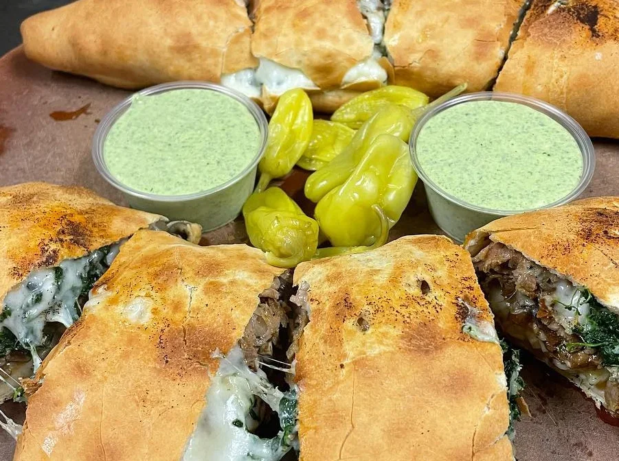 Stuffed calzones with cheese and greens served with dipping sauce and peppers