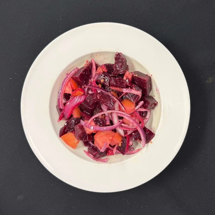 A colorful salad featuring diced beets, sliced onions, and small pieces of fruit in a white bowl.