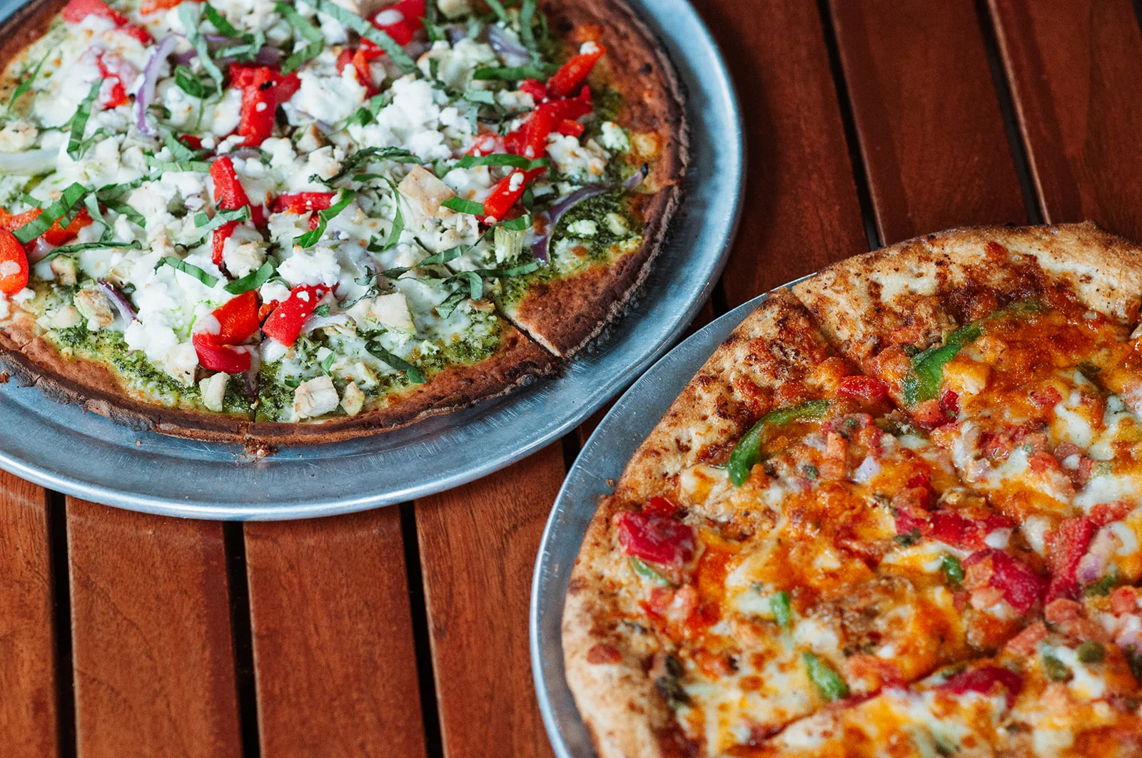 Two gourmet pizzas: one pesto chicken and one classic veggie delight.
