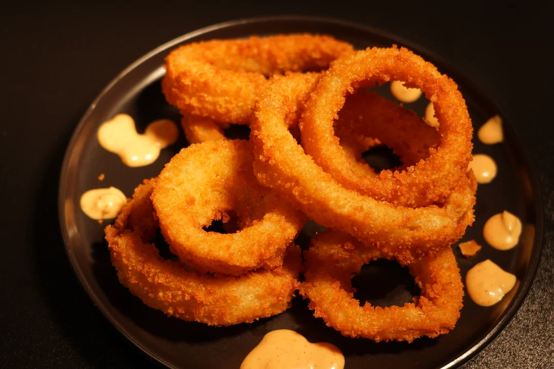 Crispy onion rings arranged on a plate with a drizzle of tangy sauce.