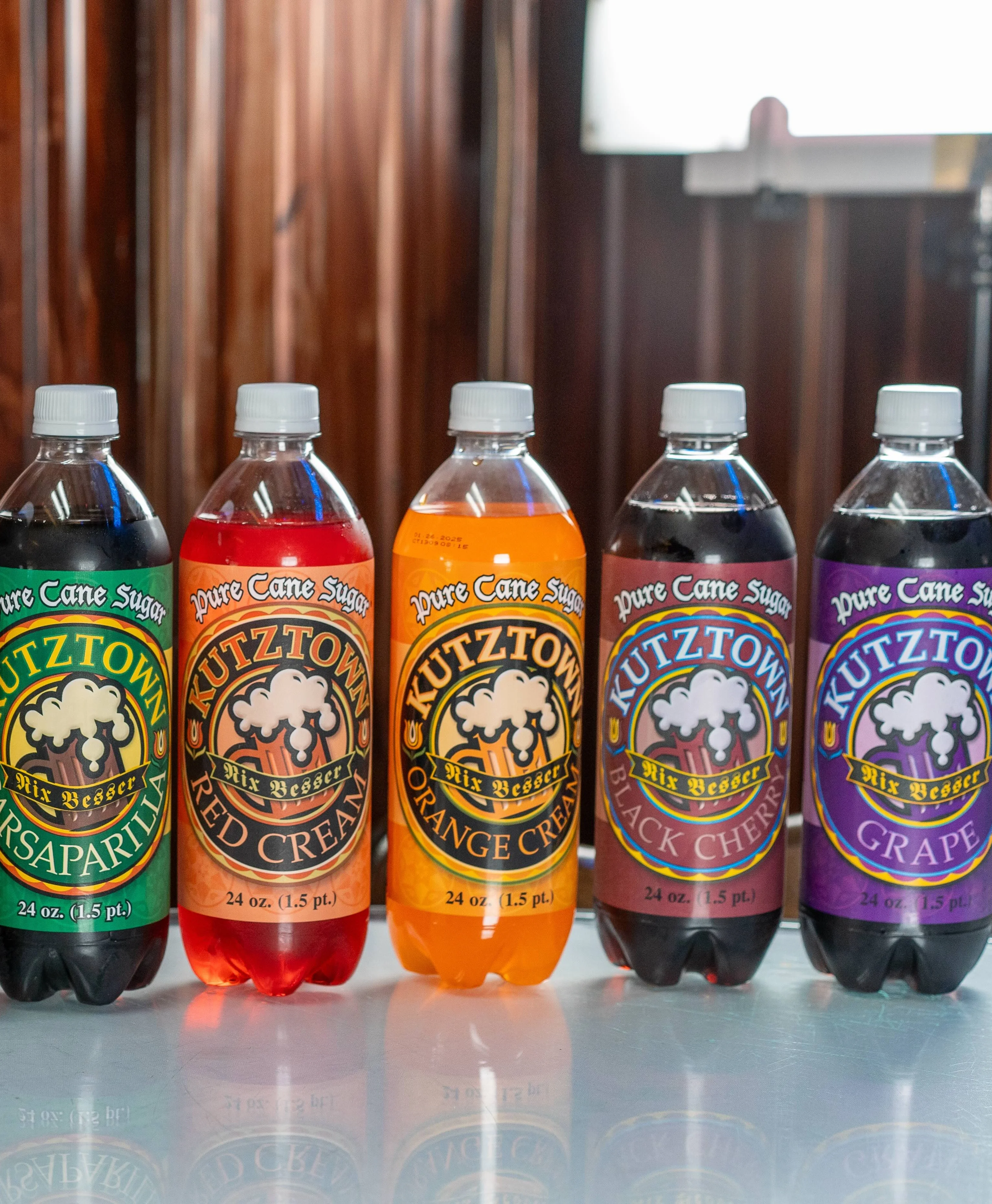 Five colorful Kutztown glass-bottle sodas lined up in front of a wood wall at Steak Out