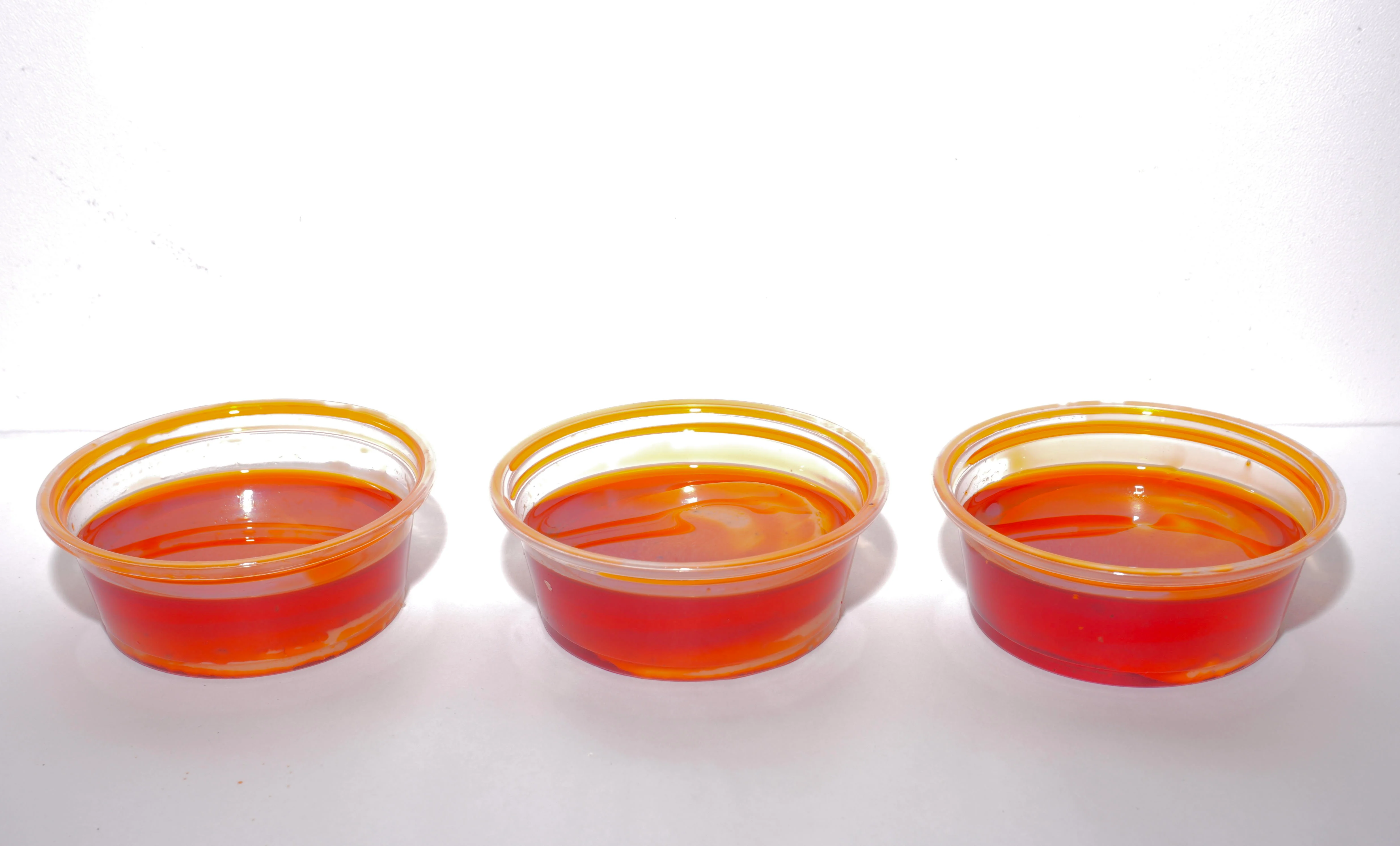 Three small clear cups filled with a vibrant orange sauce, arranged in a row against a white background.