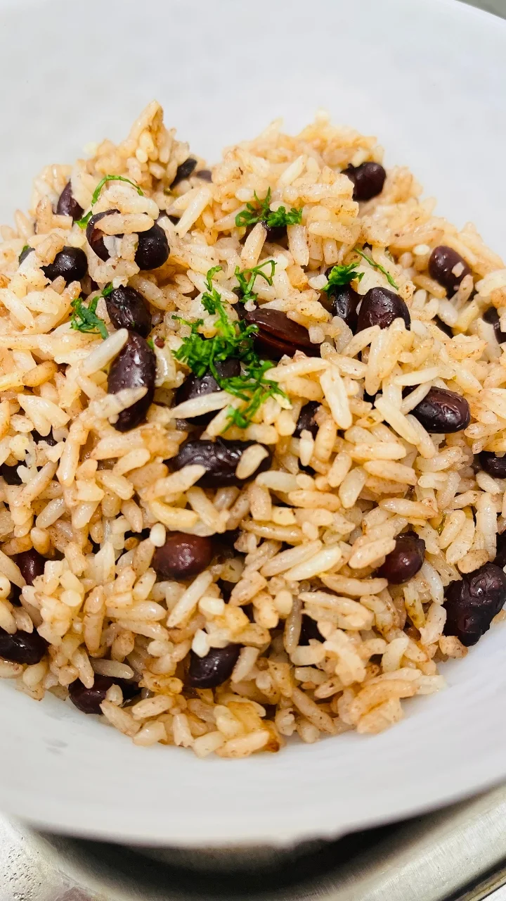 A bowl of seasoned rice mixed with black beans and garnished with fresh herbs.