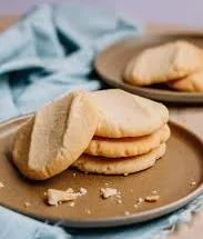 A stack of light, fluffy cookies arranged on a beige plate, with a few crumbs scattered around.