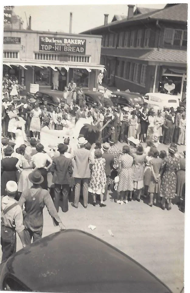 Historic street scene with crowd at bakery opening