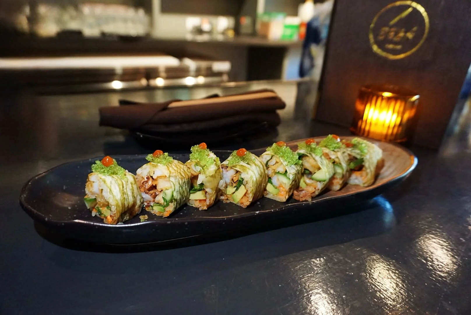 A plate of sushi rolls garnished with green toppings and orange caviar.